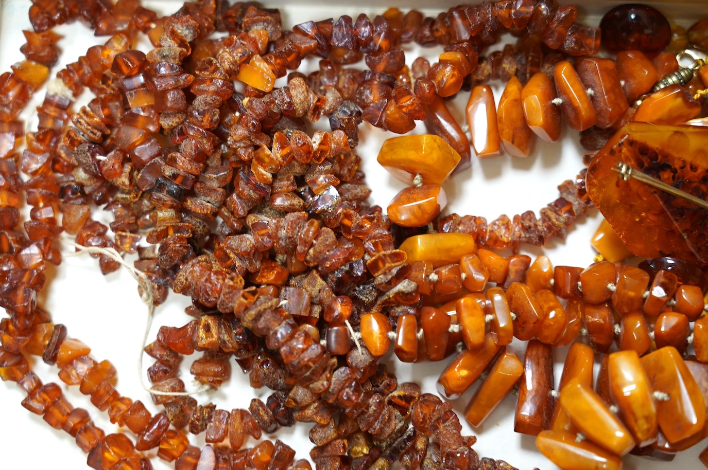 Five assorted single strand amber necklaces, including jagged pebble and unpolished, longest 176cm, together with two mounted amber rings, a pair of ear clips and a brooch, gross weight 357 grams. Condition - poor to fai